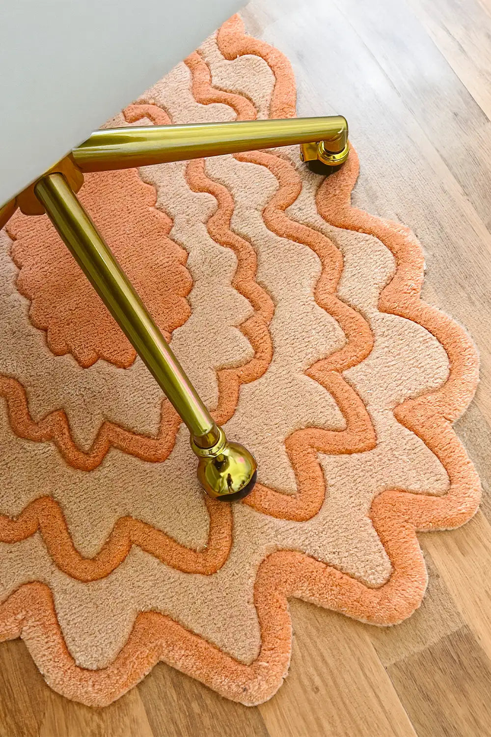 Orange ripple scalloped rug placed under gold desk chair, funky oval wool rug in modern office