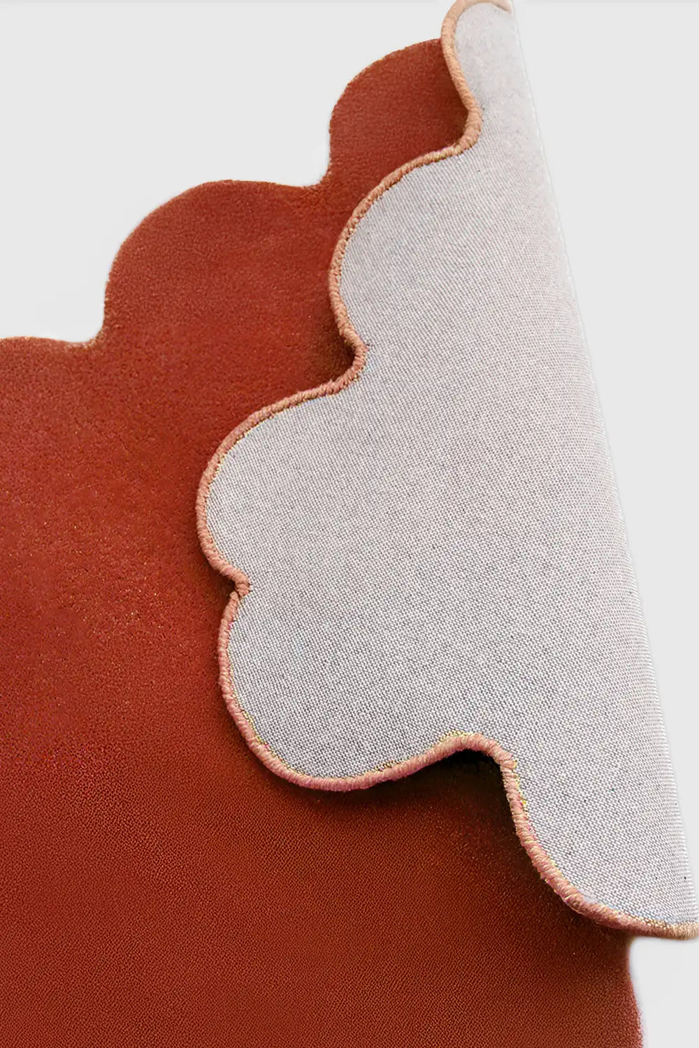 Orange terracotta scalloped edge wool rug folded to reveal cotton backing and sculpted hand-carved shape