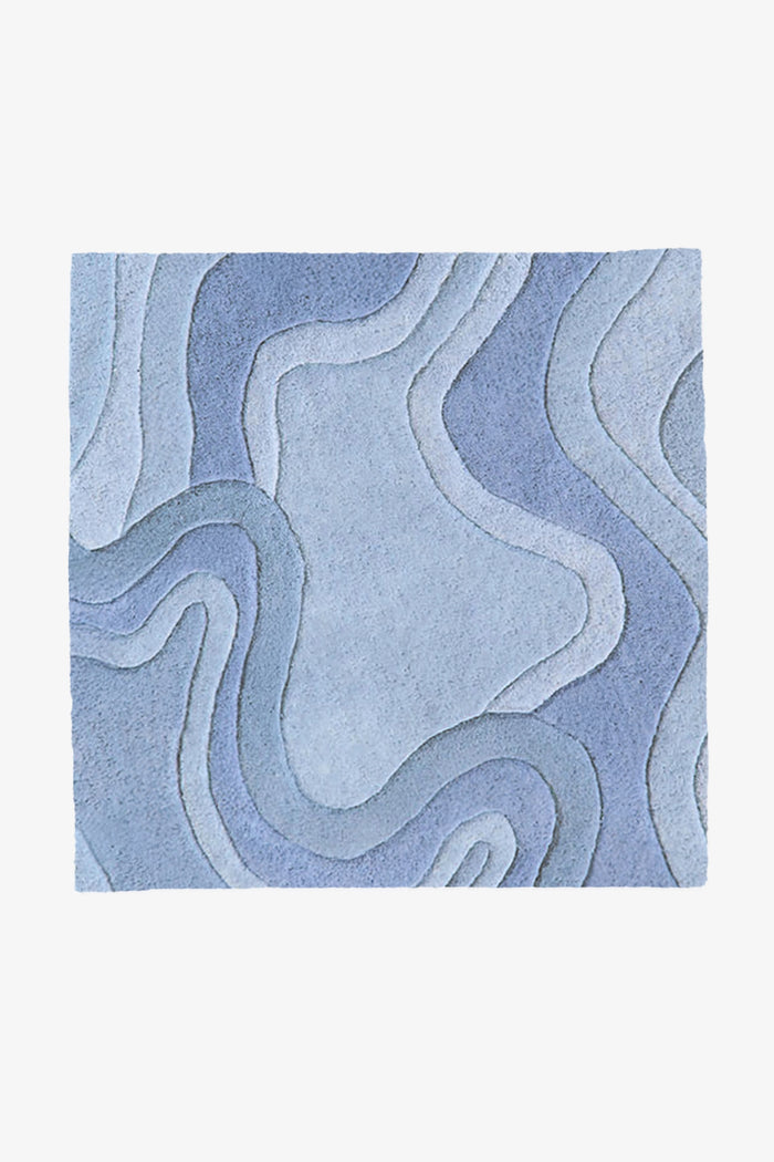 A square area rug with an abstract, layered topographic pattern in various shades of blue and light gray, shown flat against a light gray background.