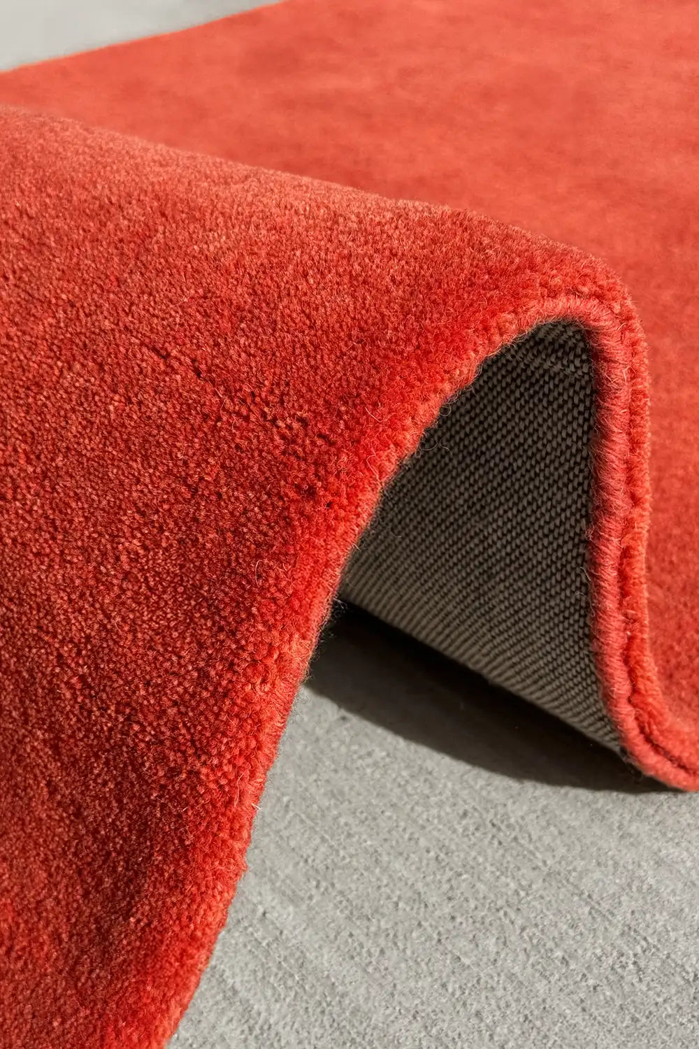 Close-up of a bold red orange textured wool rug on a gray surface