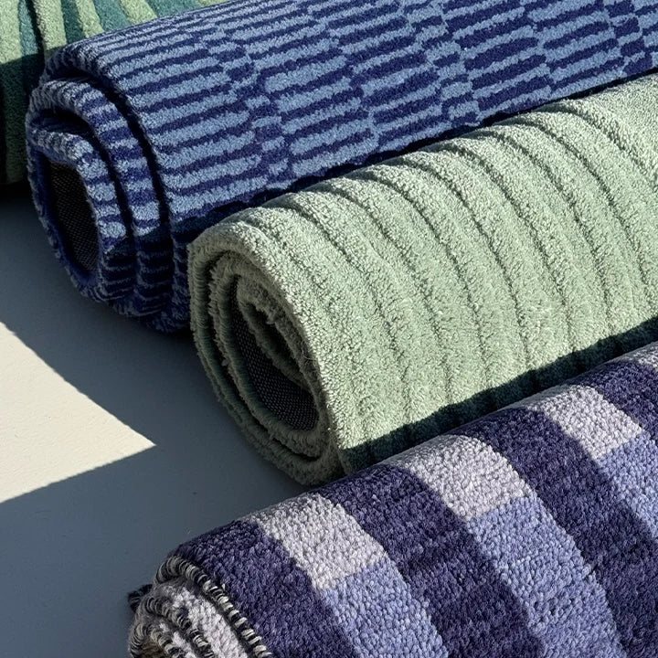 Three rolled-up rugs in blue, green, and multicolor patterns on a gray surface.