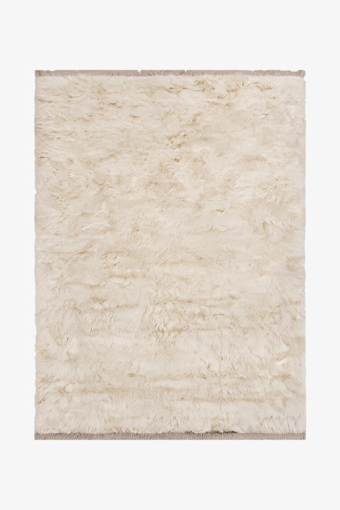 A rectangular shaggy area rug in a warm cream or off-white color, shown flat against a plain white background.