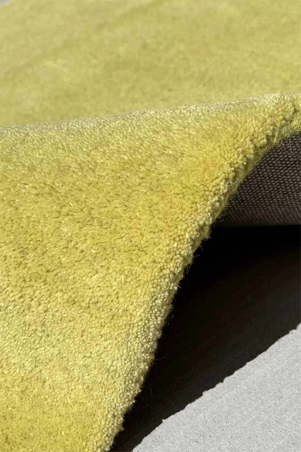 light green soft wool rug shown with corner lifted to display thick pile and durable backing