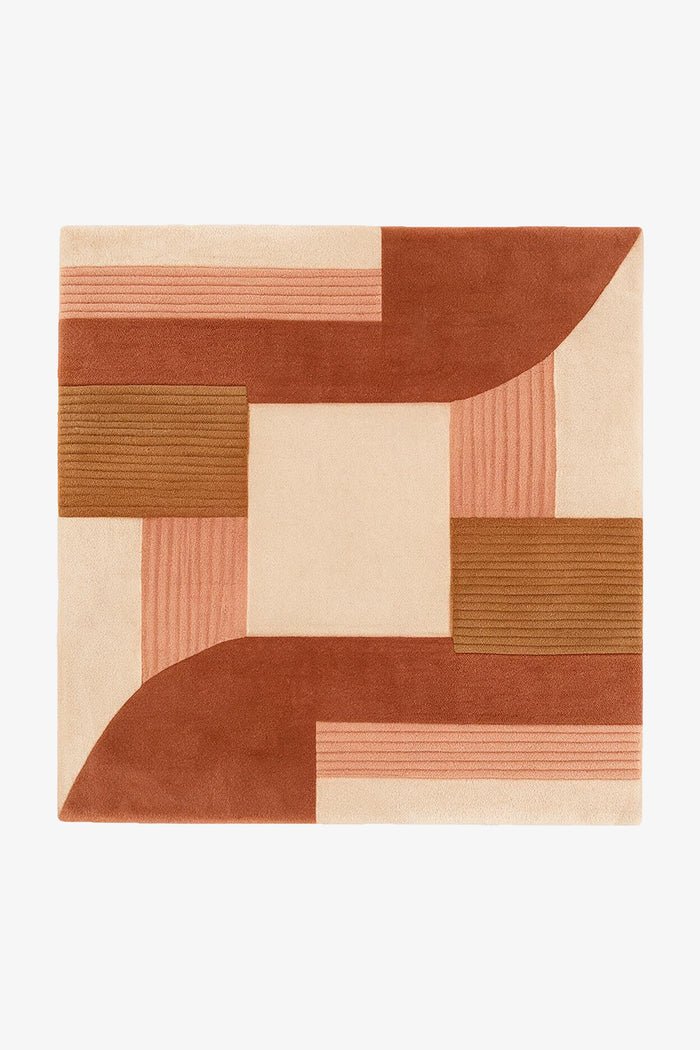 A square area rug with an abstract geometric pattern in terracotta, rust, peach, and cream, shown flat against a plain white background.