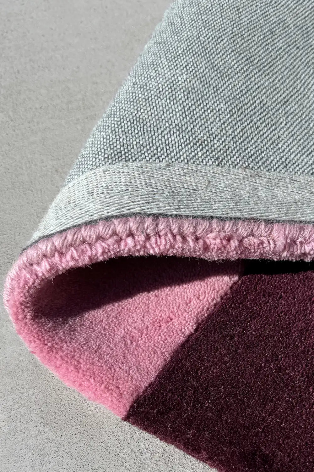 Rolled corner of deep purple and pink wool rug, showcasing plush texture and clean finish for modern interiors