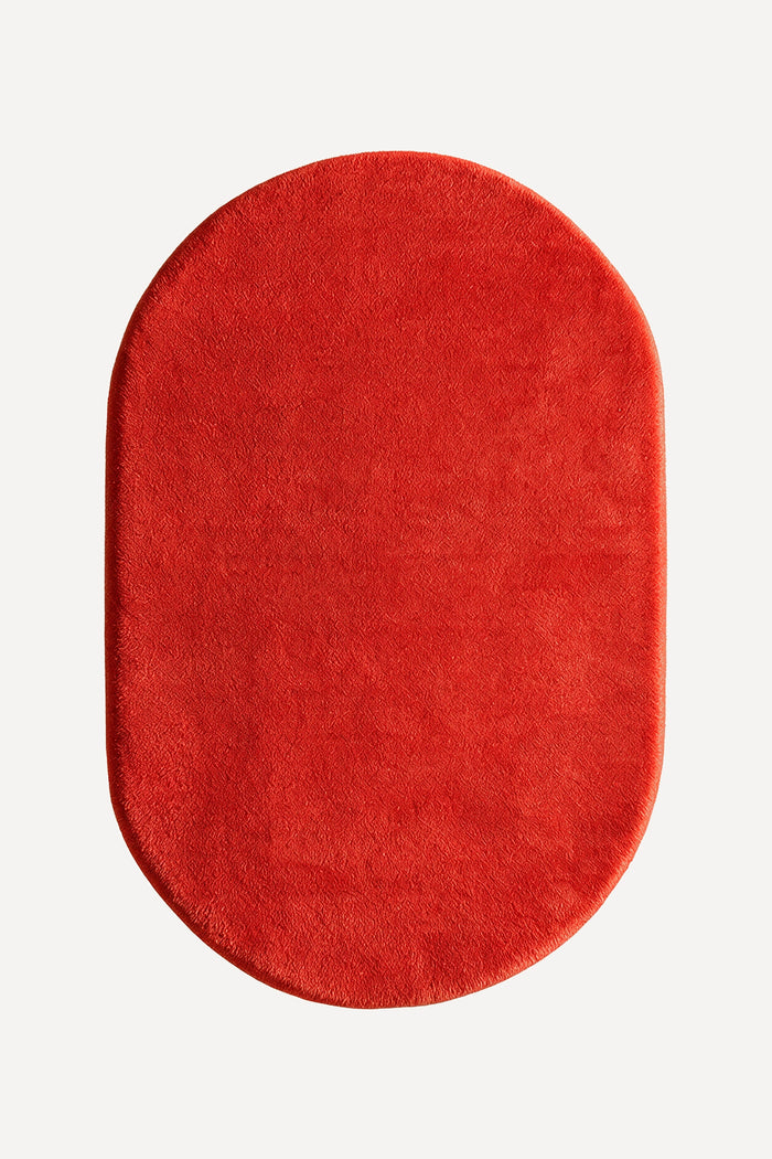 A vibrant red oval rug with a plush, soft texture, shown from a top-down view on a light gray background.