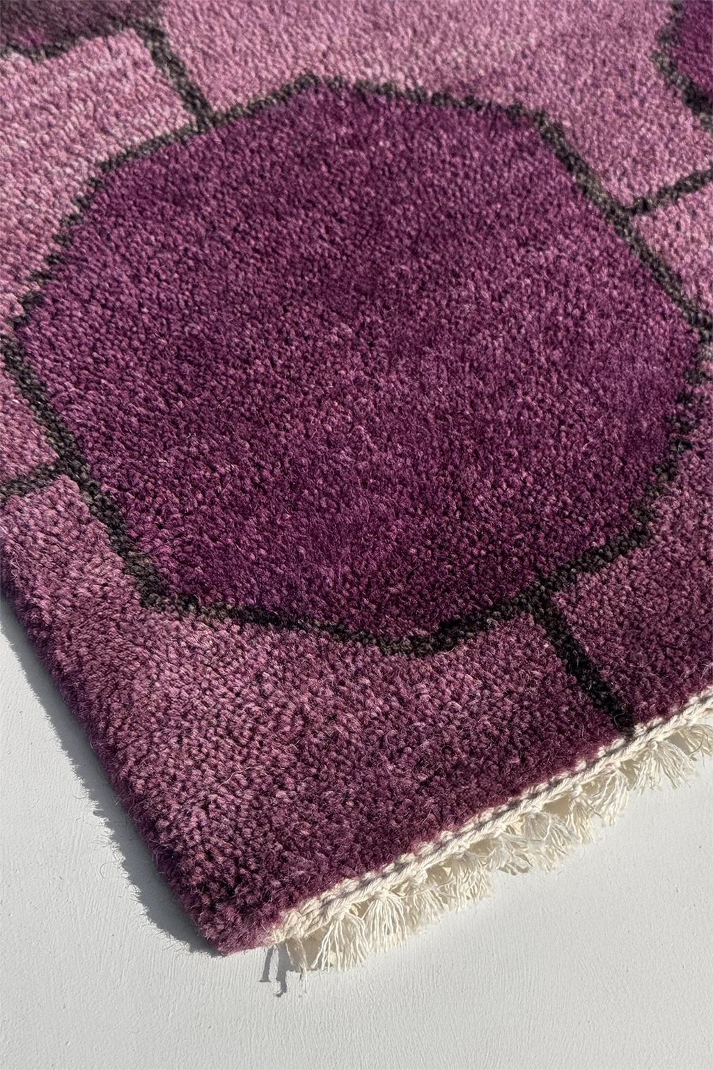 Close-up of a purple textured wool rug with geometric pattern on a light gray background