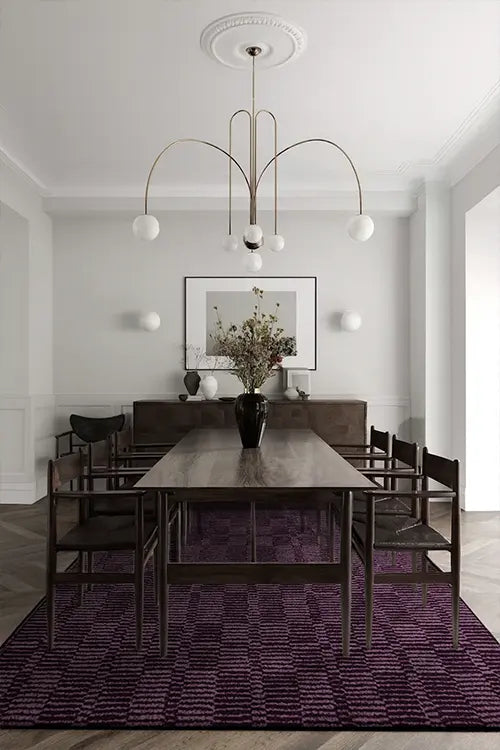 Dining room with a long wooden table and chairs on a custom purple 8x10 wool rug, featuring a modern chandelier and a framed picture on the wall.