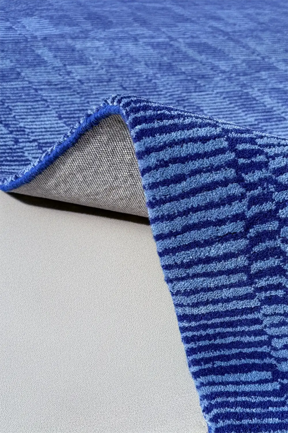 Luxury wool rug in blue, shown folded to reveal edge detail and backing material