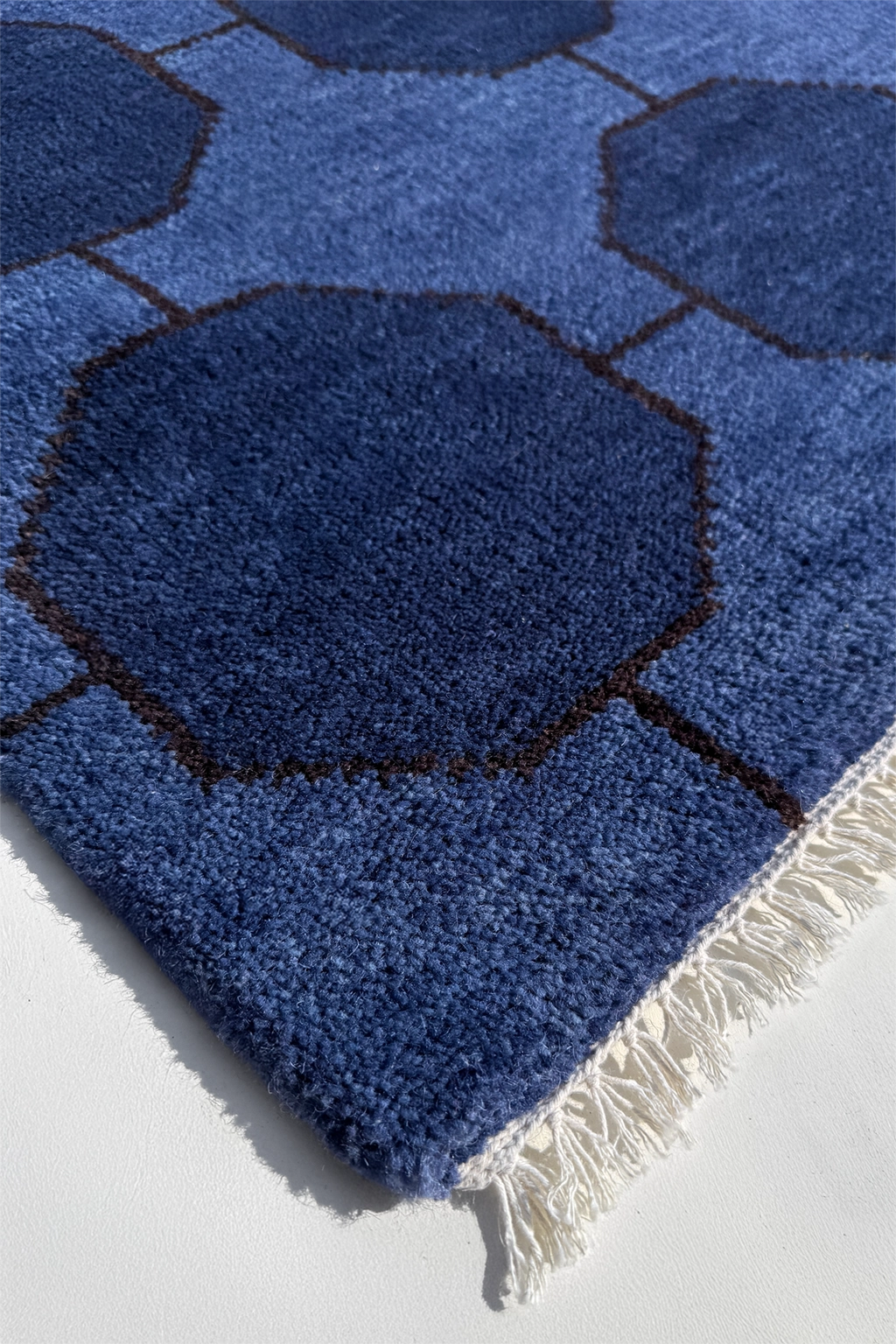 Modern blue geometric patterned rug with white fringe on a light gray background