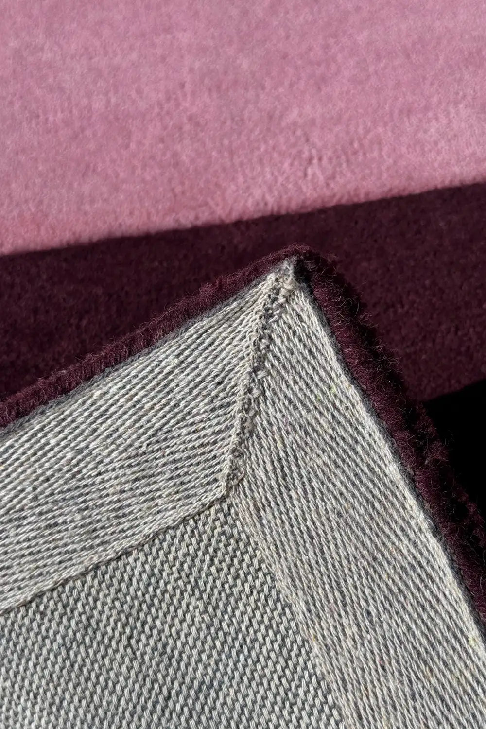 Blush and plum pink rug corner flipped to show stitched edge and backing, handmade wool rug for living room