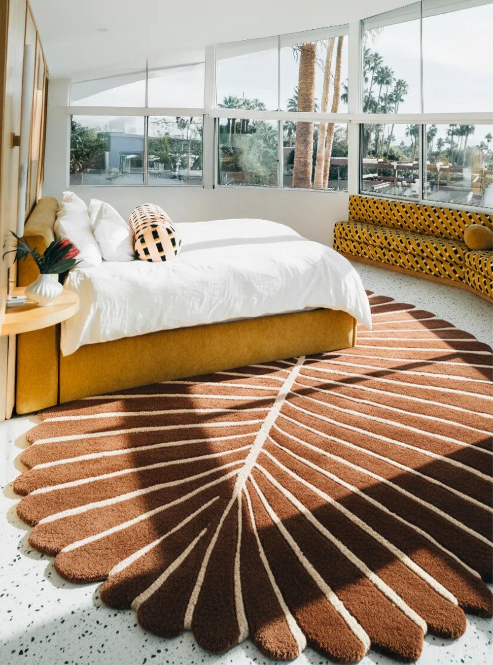 Modern bedroom with a large palm leaf patterned rug, bed, and window view.