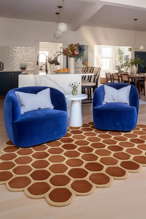 Two blue chairs with white pillows on a brown geometric-patterned rug in a modern living room.