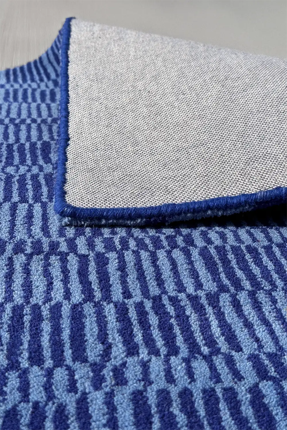 Reverse side of navy blue geometric wool rug with durable grey cotton backing and precision edge finish