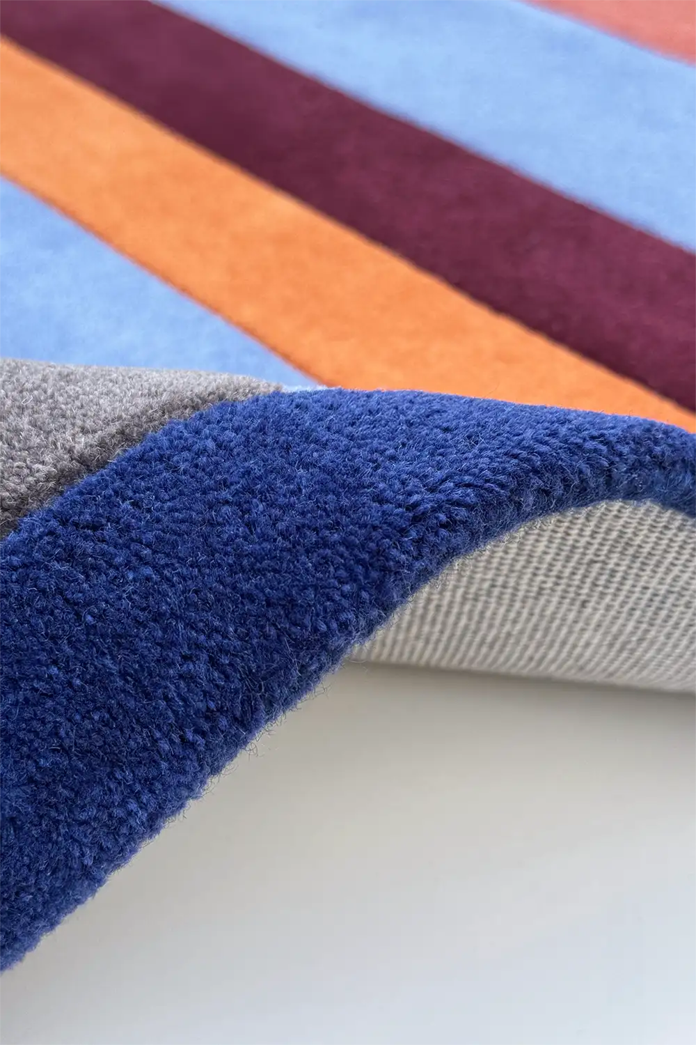 Close-up of a multicolored striped rug with blue, orange, maroon, and gray sections.