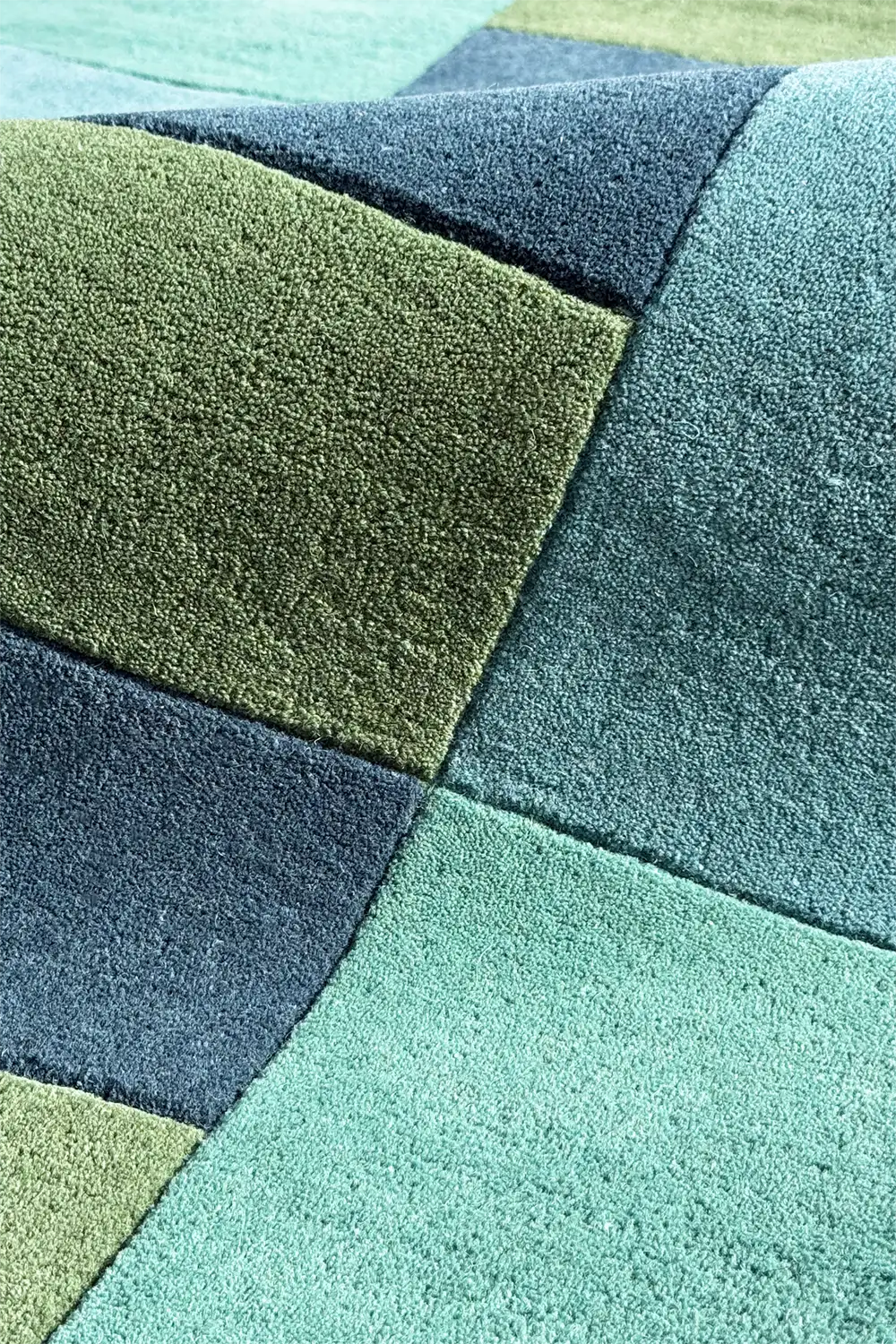 Colorful geometric wool rug with overlapping blocks in teal, navy, sage, and aqua tones