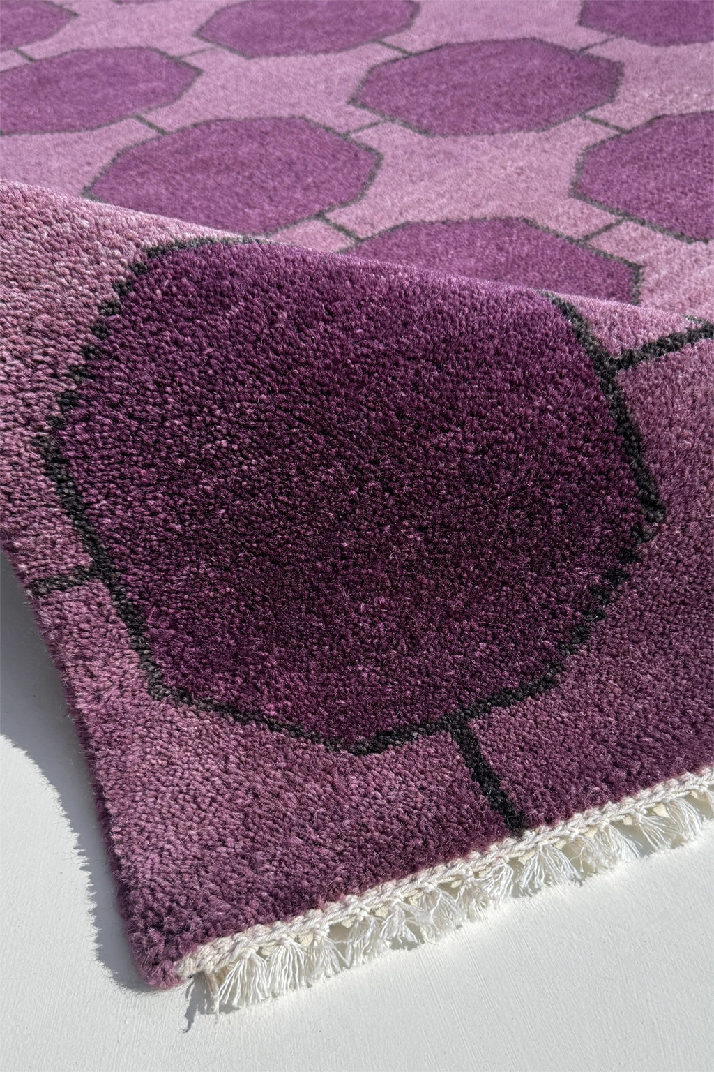 Close-up of a purple hand-knotted rug texture with geometric pattern on a white background