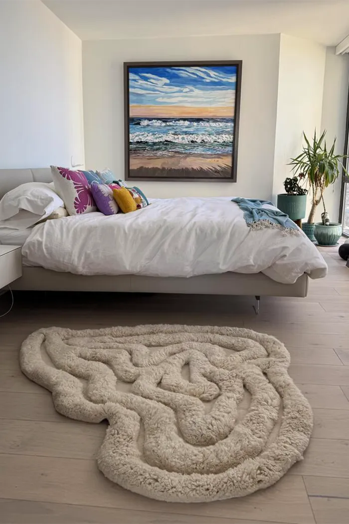 Cream-toned sculpted wool rug with fluid organic lines, shown in a minimalist high-rise bedroom