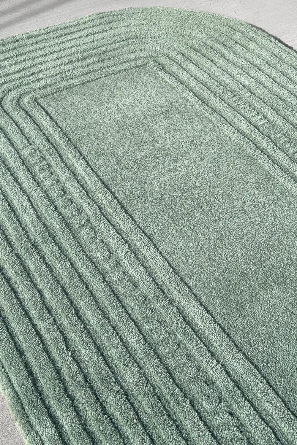 Angled view of carved sage green wool rug with concentric border, a calming japandi-style option for boho chic bedrooms
