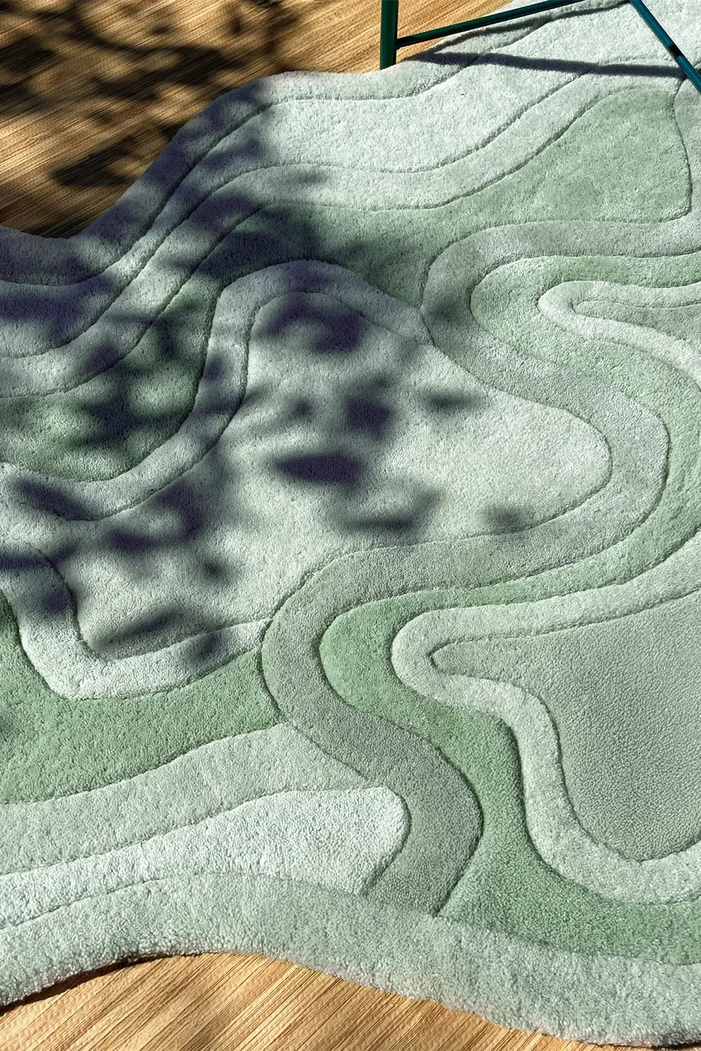 Sage green irregular shaped wool rug with carved curves, styled outdoors with natural shadow play