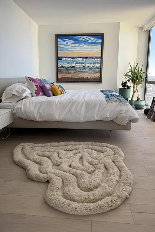 Modern bedroom with a bed, decorative pillows, and a large white organic-shaped shaggy rug.