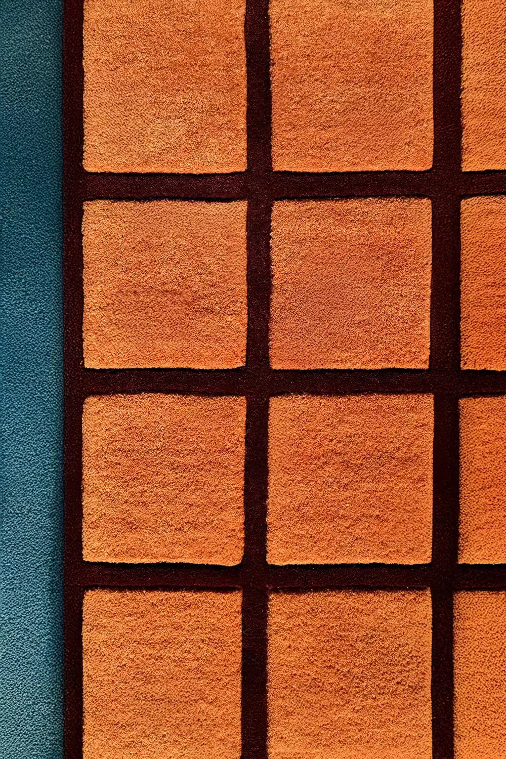 close up texture of orange and burgundy wool square tufted rug with grid pattern