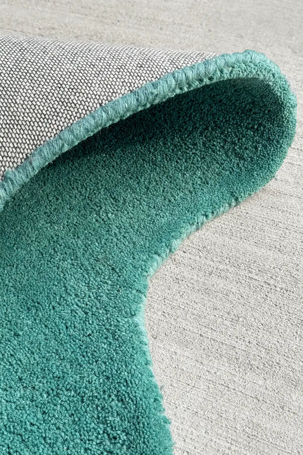Rolled edge detail highlighting plush wool texture and irregular shape of this scalloped teal rug, great for cool modern spaces