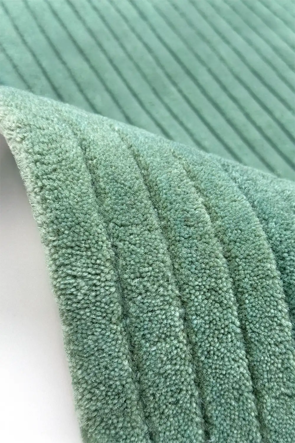 Close-up of teal textured wool rug hand tufted on a white background