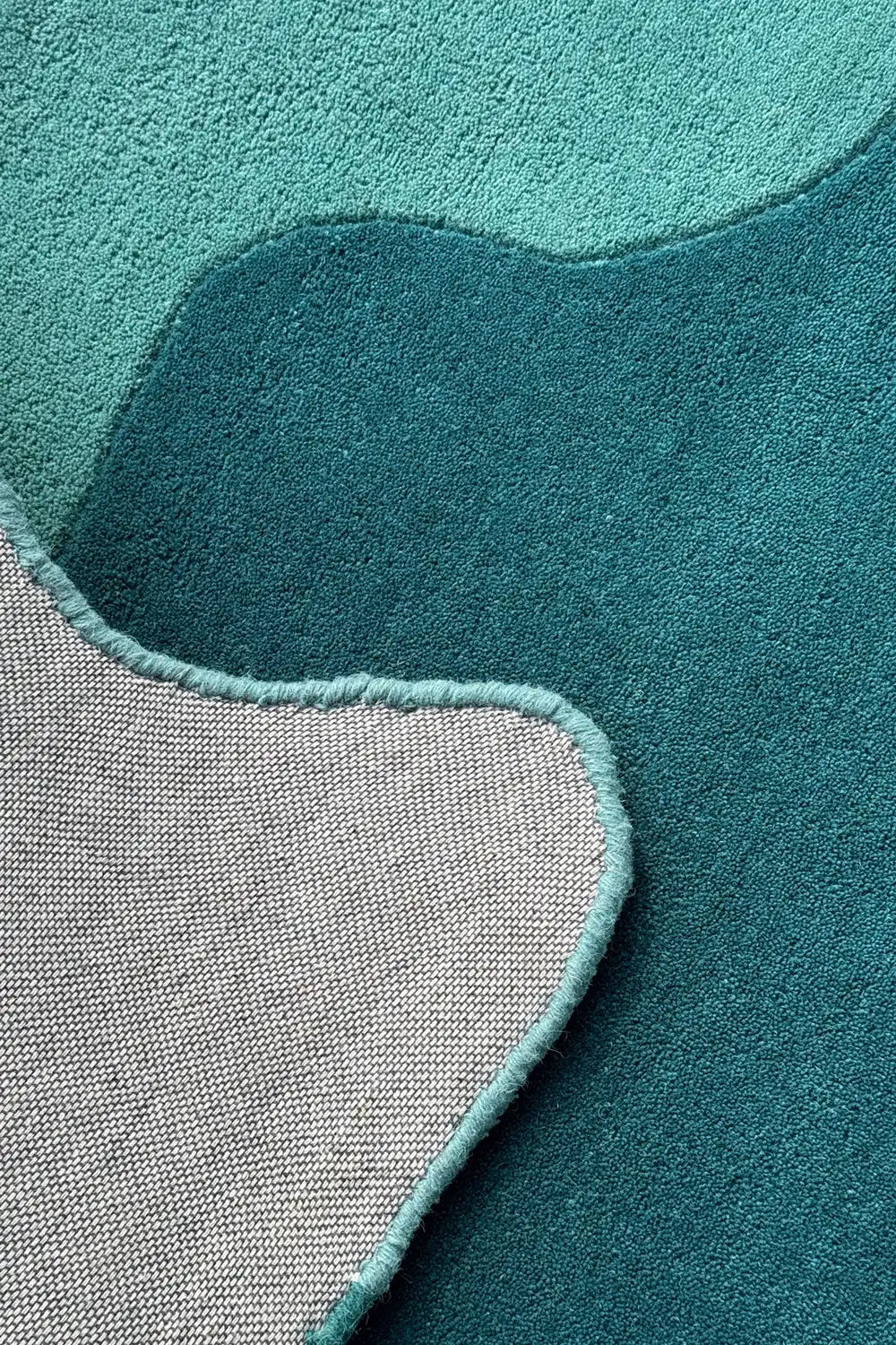 Soft turquoise curve with carved detailing on irregular rug corner, perfect as a whimsical carpet design for modern interiors