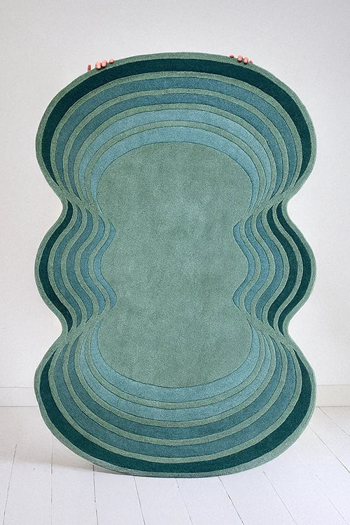 Rounded, multicolored rug with wavy pattern held up in a studio