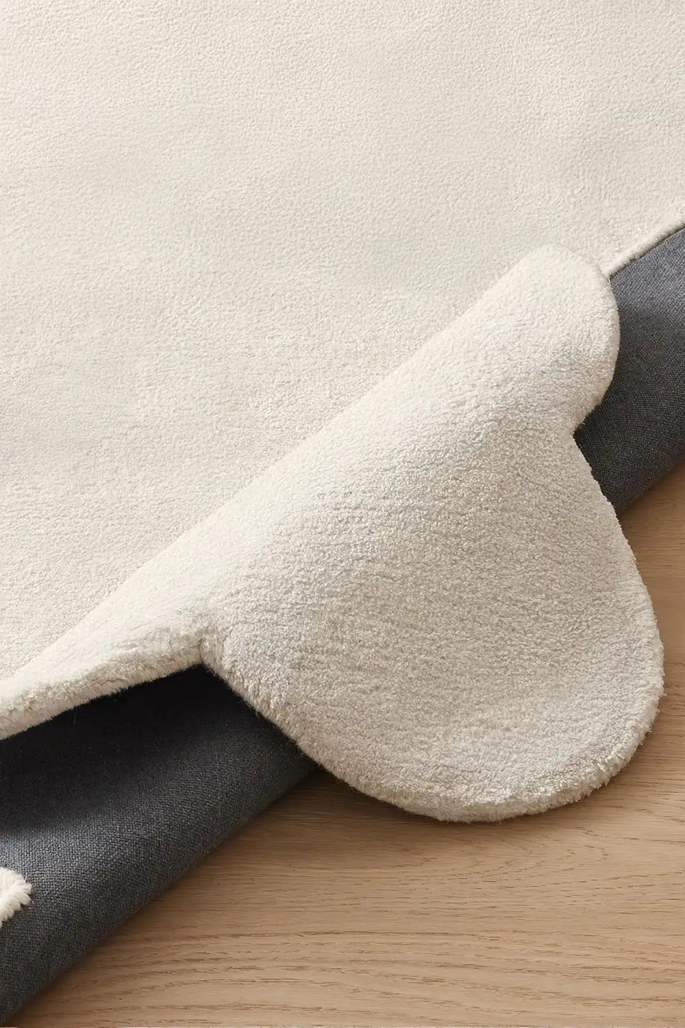 Close-up of plush cream wool rug with scalloped border, featuring soft hand-tufted pile and durable backing