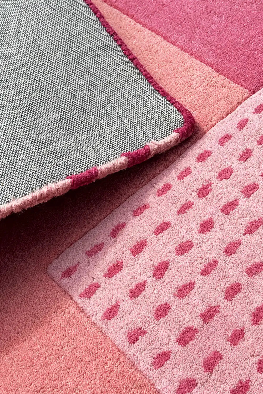 Folded corner of graphic pink wool rug showing cotton backing, hand-tufted texture, and block color detail