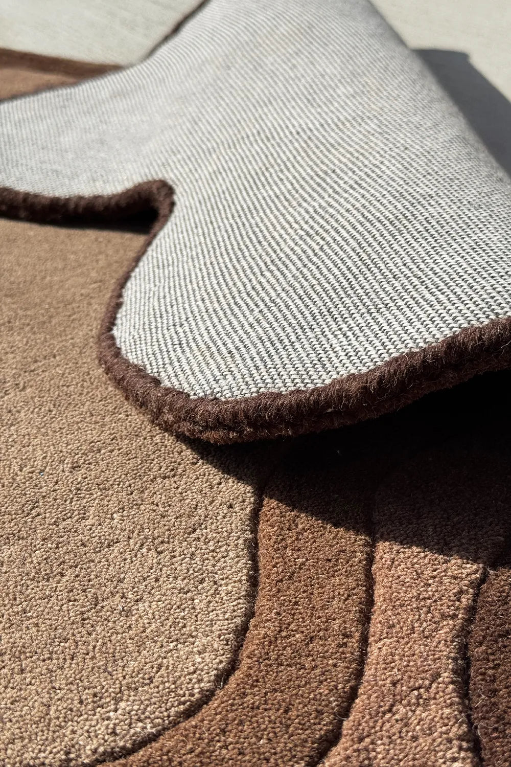 Tufted handmade brown area rug with organic silhouette featuring soft sculptural texture and neutral palette for cozy modern homes