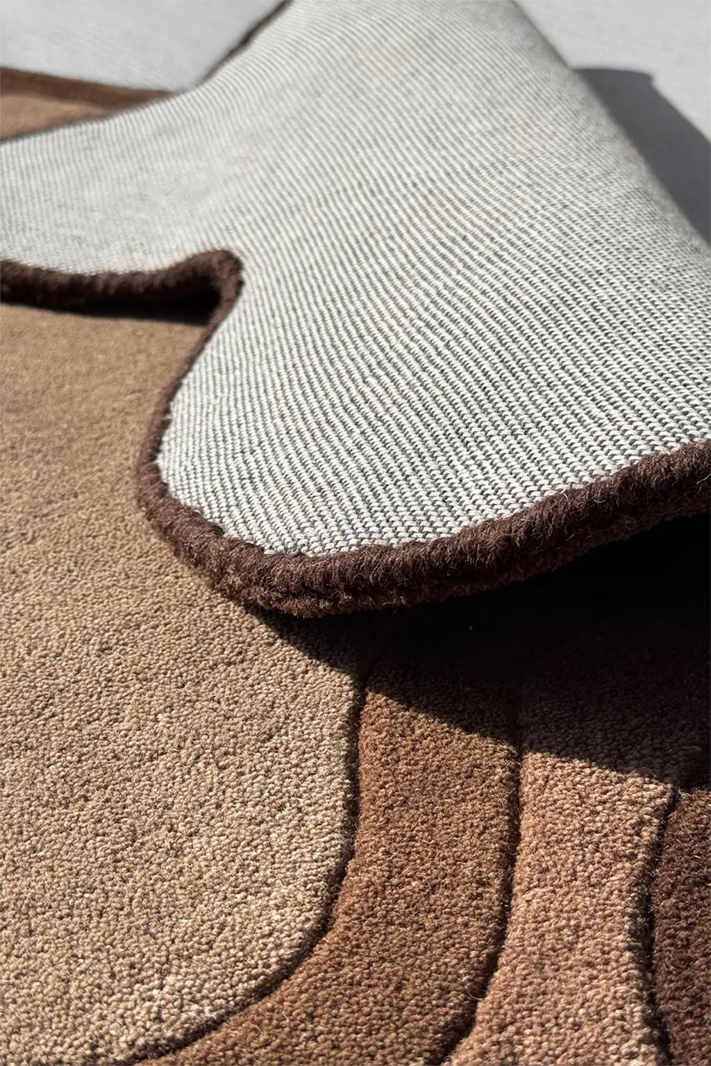 Tufted handmade brown area rug with organic silhouette featuring soft sculptural texture and neutral palette for cozy modern homes