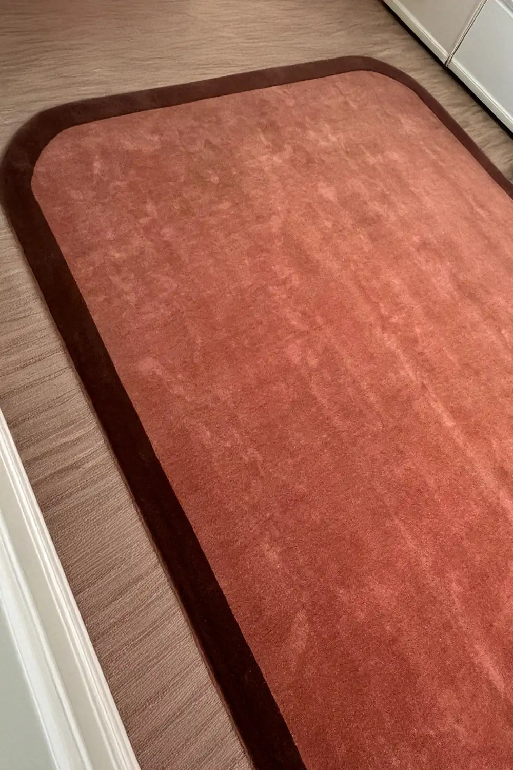 A side perspective of the brown contour edge rug, emphasizing the flowing, curved border and rich wool material.