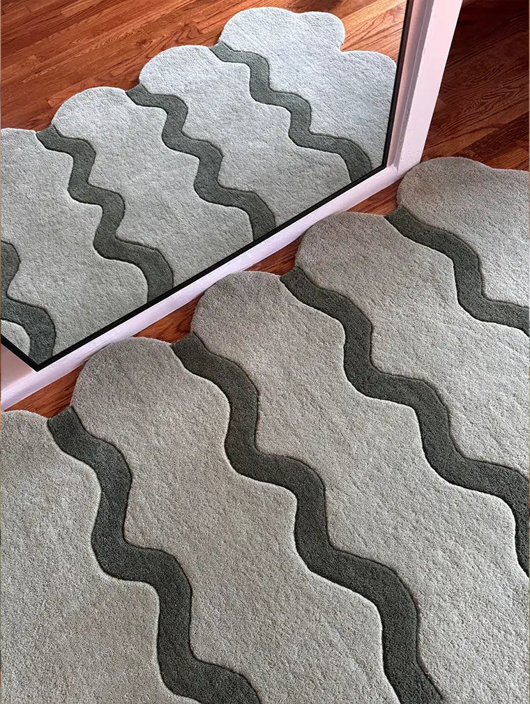 Close-up of a sage green ripple scalloped rug reflecting in a mirror, highlighting its intricate tufted design and soft texture.