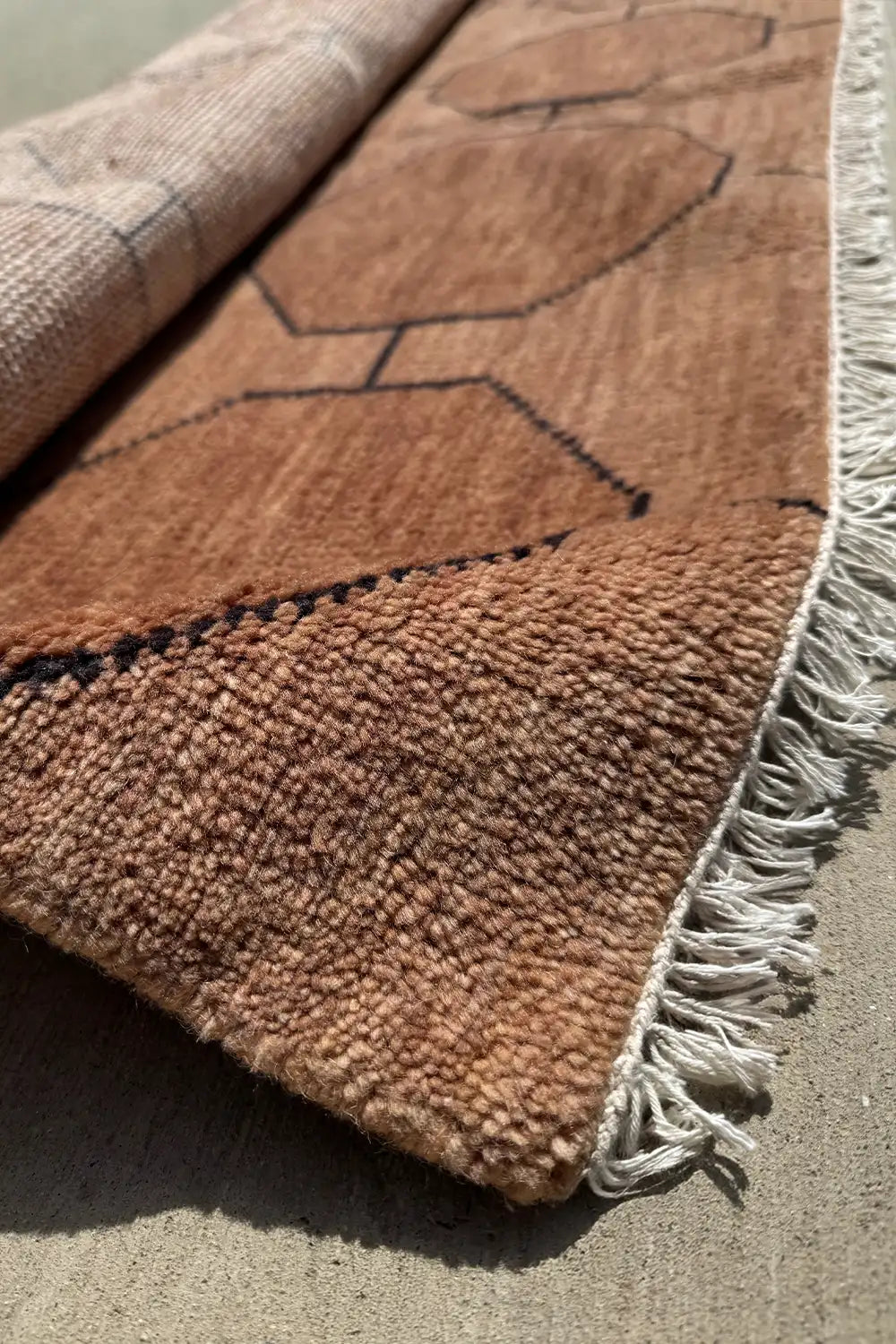 Corner detail of brown living room rugs showing fringe and octagon design hand knotted from textured wool