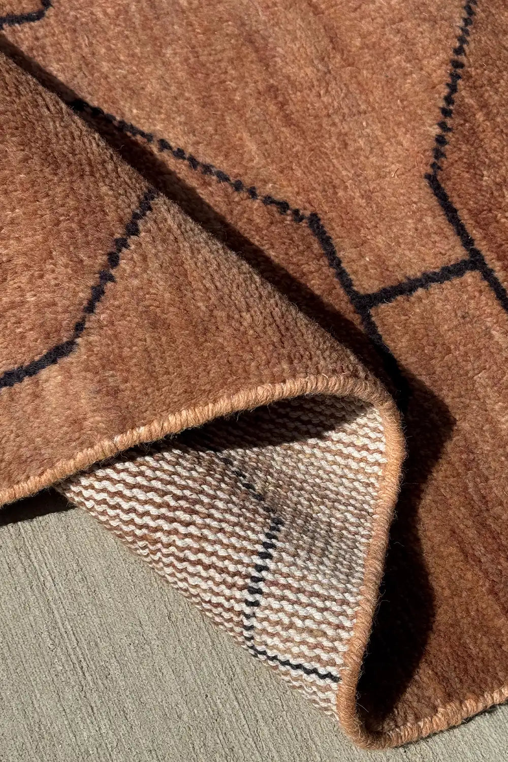 Rolled edge of 5x8 brown knotted rug highlighting high quality weave and earth-toned texture