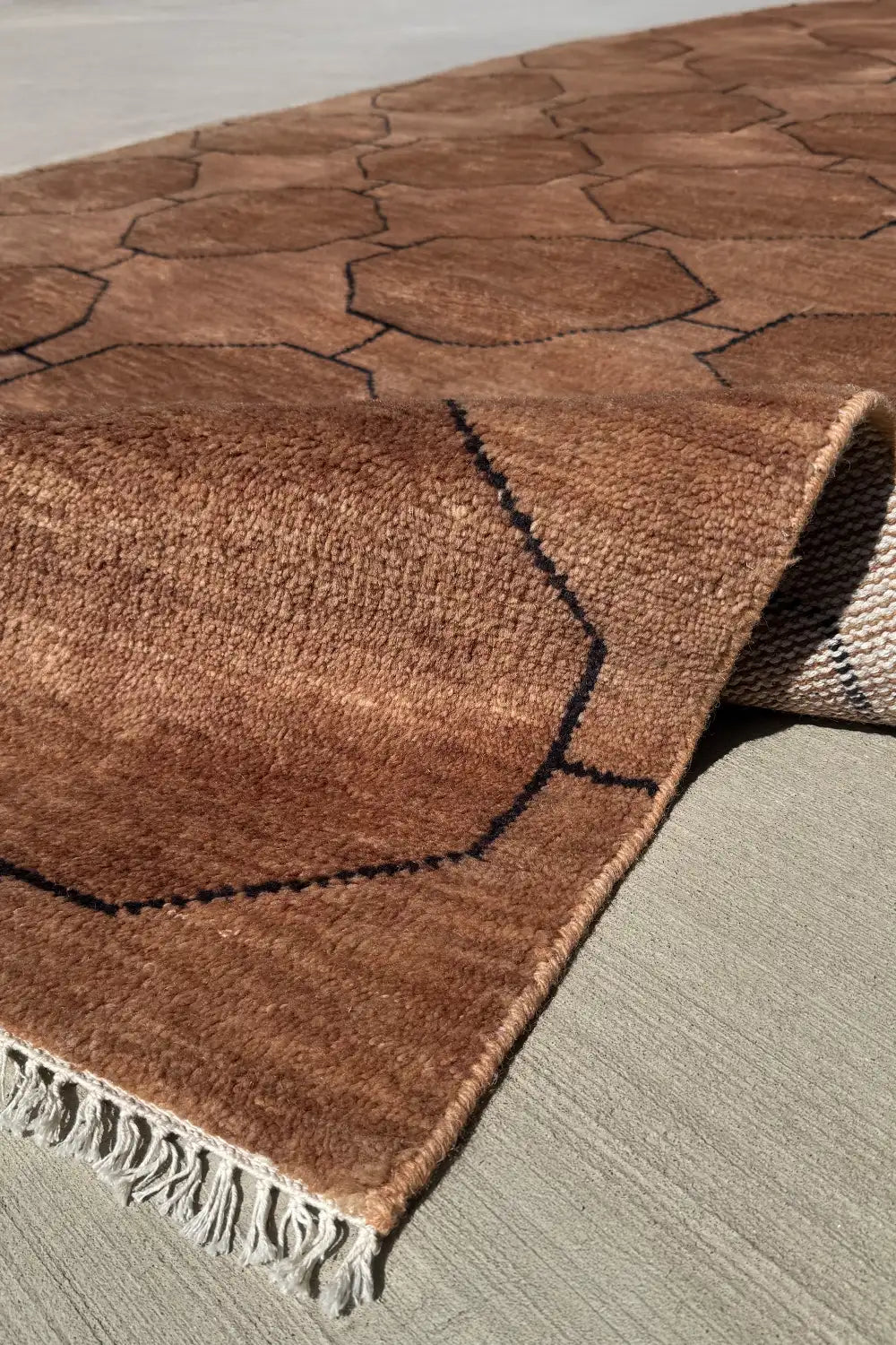 Angled view of a 6x9 brown geometric wool rug showing thickness, fringe, and soft surface texture