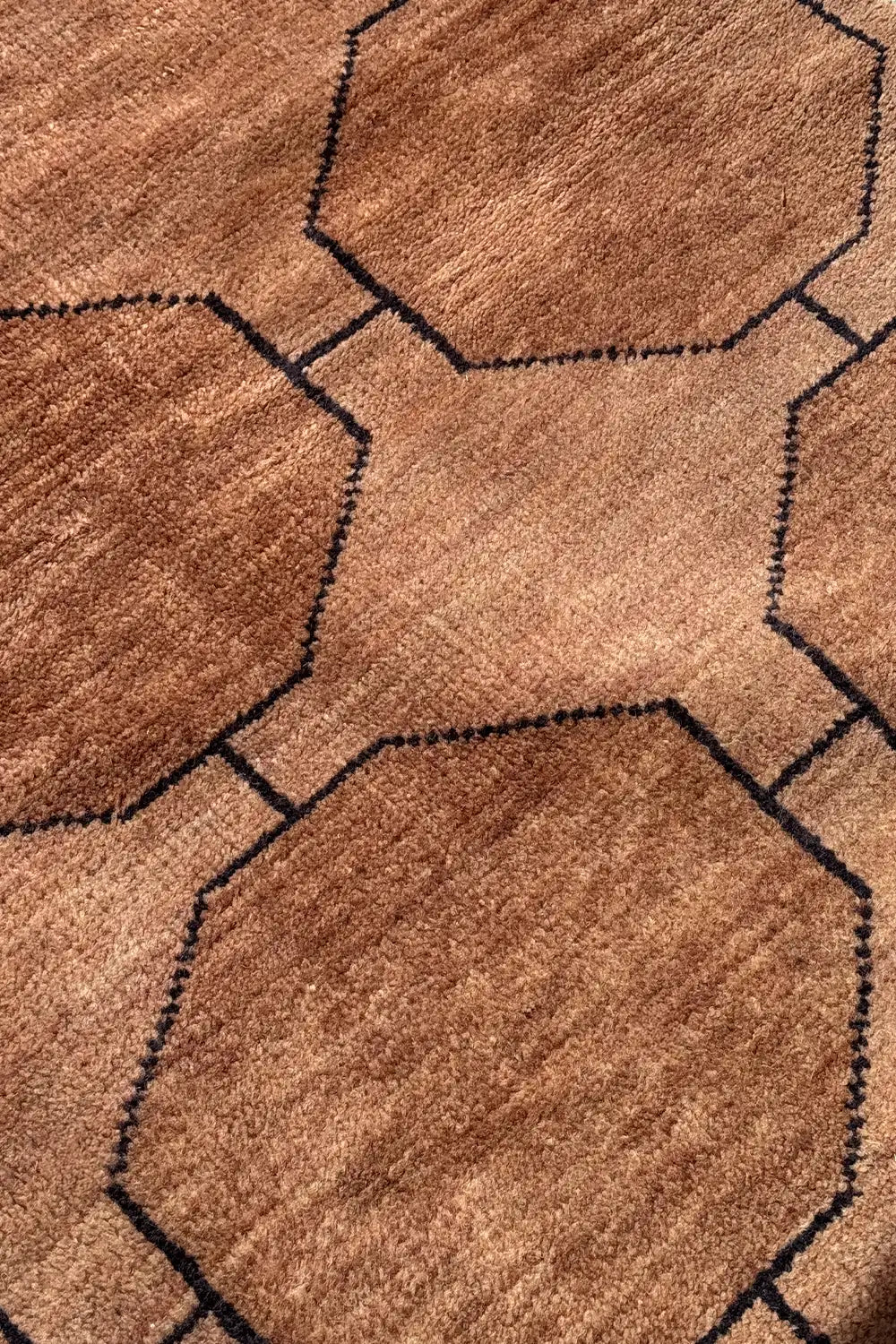 Macro shot of a geometric light brown hand knotted area rug showing texture and contrast stitching