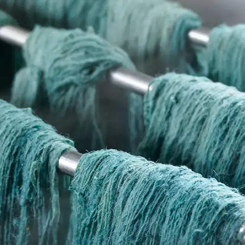 Freshly dyed teal wool strands hanging to dry, part of the traditional rug-making process.
