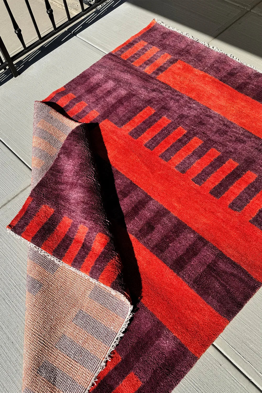 Hand-knotted red wool rug with a bold geometric pattern in deep burgundy and burnt orange hues