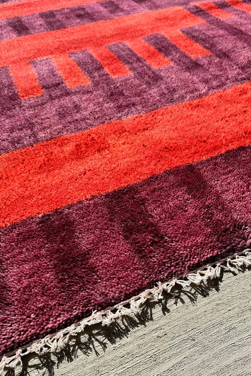Artisan-crafted red geometric rug with a bold striped pattern in burnt orange and aubergine