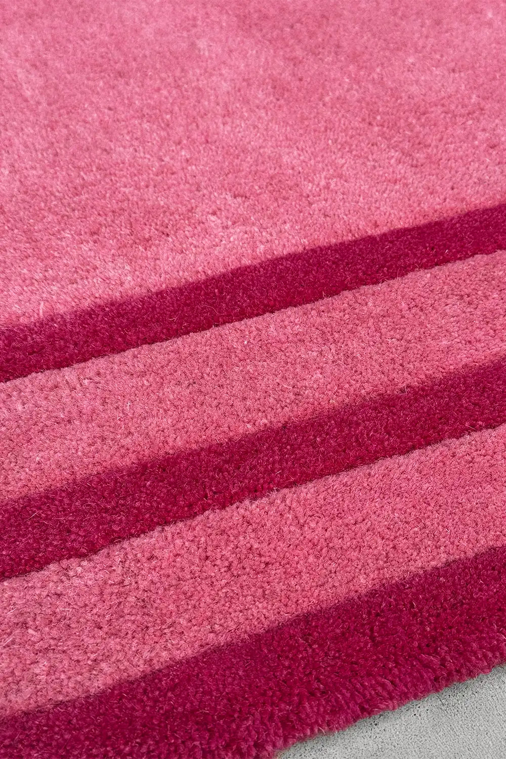 Close-up of tufted pink wool rug with thick stripe detail in rose and fuchsia, hand-carved for texture