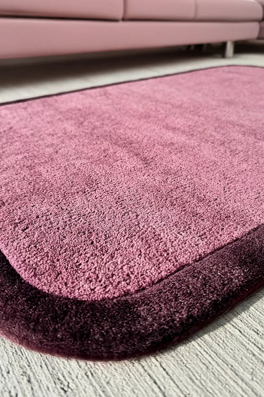 A close-up of a purple wool rug with a sculptural contour edge, featuring deep color tones and a thick, plush border.