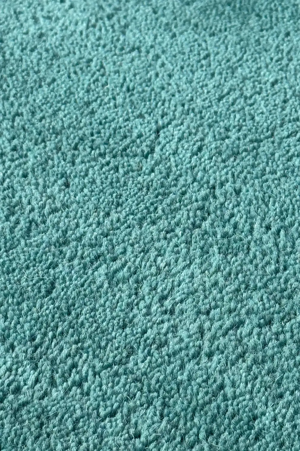 Close-up of teal tufted wool rug surface showing soft plush pile and dense texture