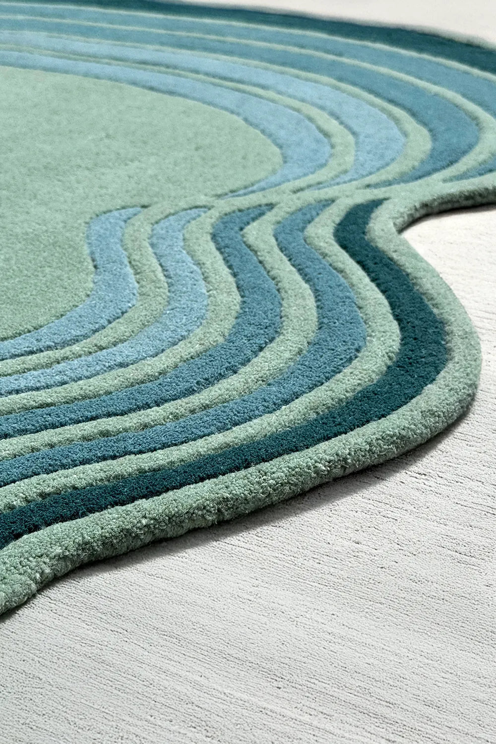 Tufted sculptural edge of green and blue rug, a unique shaped wool rug with funky wavy design for playful spaces