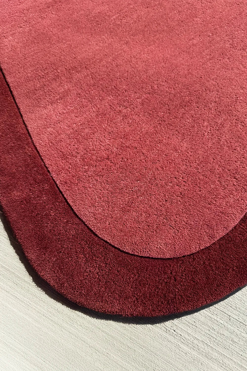 Curved corner of a 4x6 red abstract wool rug with an organic, sculpted shape in burnt orange and burgundy tones