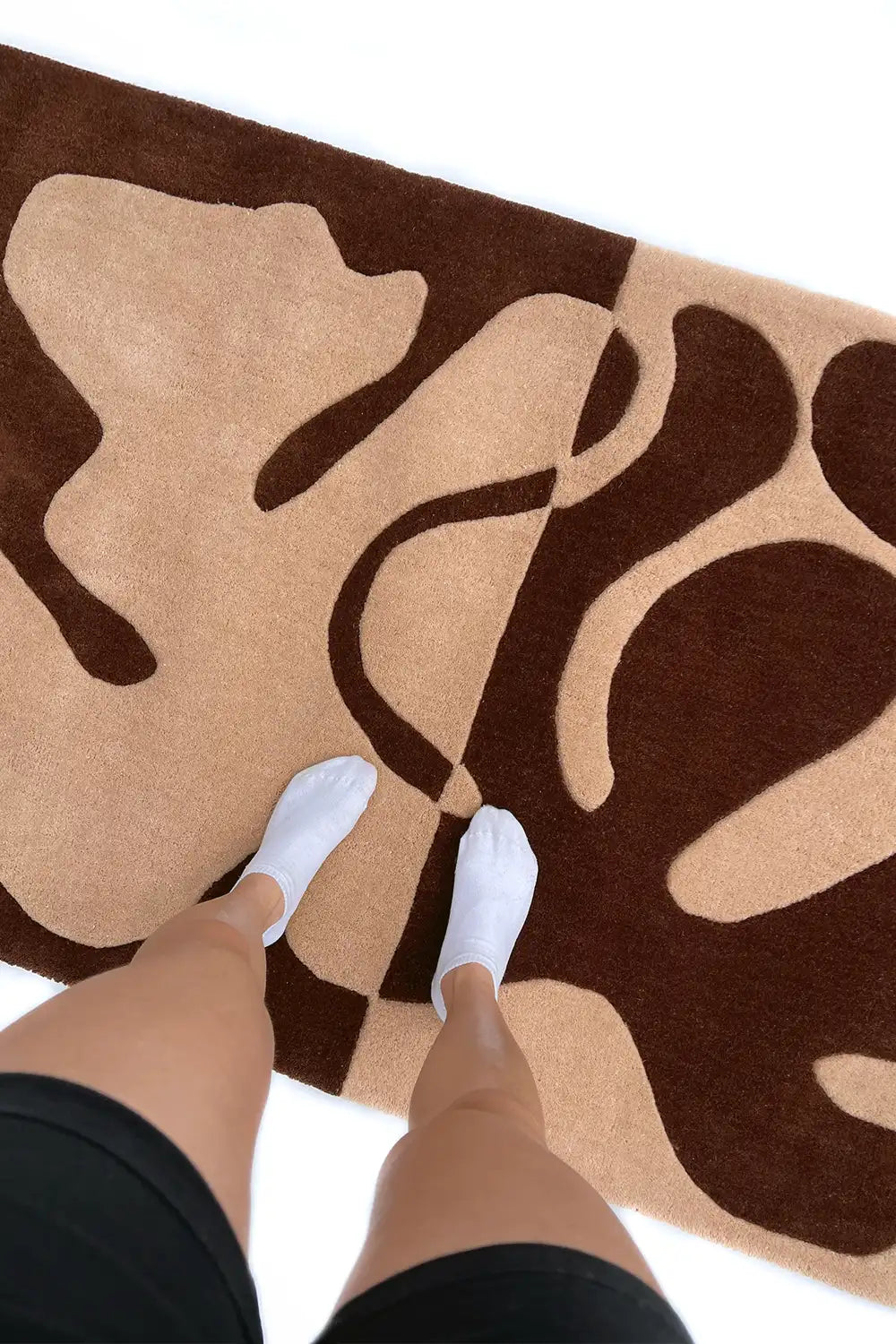 Feet stepping on plush hand-tufted brown and cream abstract rug lifestyle