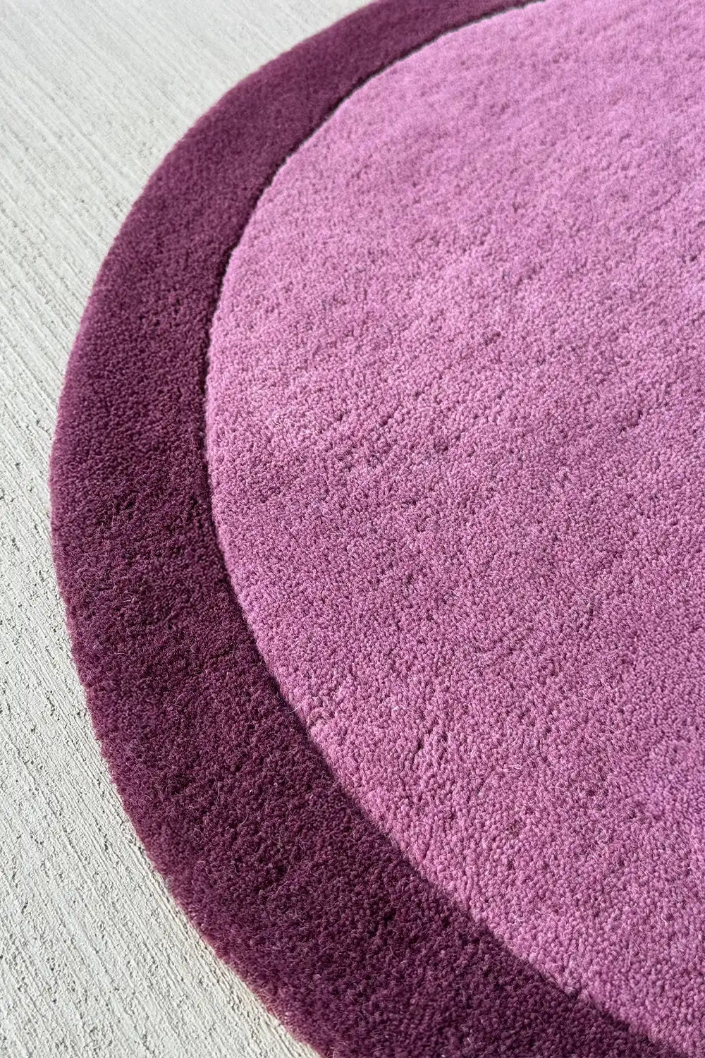 Curved edge of purple irregular shaped round wool rug with a soft plush texture